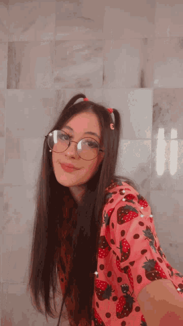 a girl wearing glasses and a pink shirt with strawberries on it sticks her tongue out