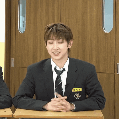 a man in a suit and tie with a name tag that says nb sits at a desk