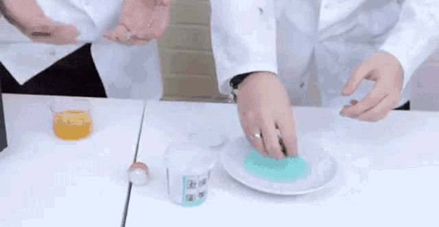 a person in a lab coat is holding a green substance on a white plate on a table .