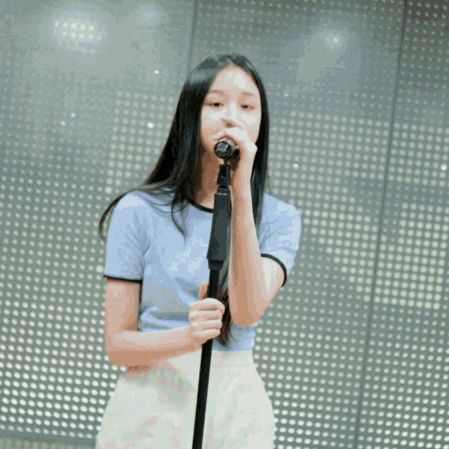 a young girl singing into a microphone in front of a wall with dots on it