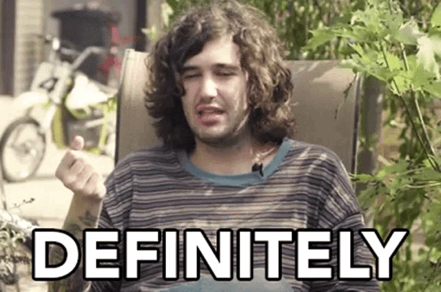 a man with long curly hair is sitting in a chair with the word definitely behind him