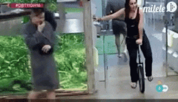 a woman is riding a unicycle in a hallway next to a man .