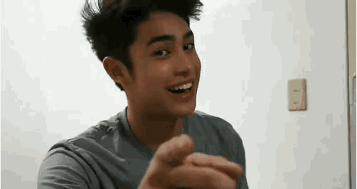 a young man is smiling and pointing at the camera while wearing a grey shirt .