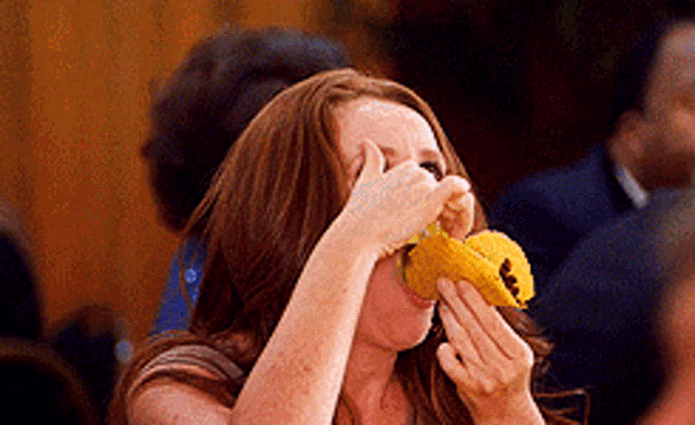 a woman with red hair is eating a yellow item with a smiley face on it