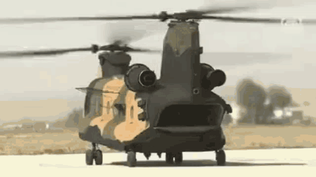 a military helicopter is sitting on a runway in a field .