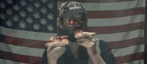 a man wearing a hat that says whiskey is eating a slice of pizza