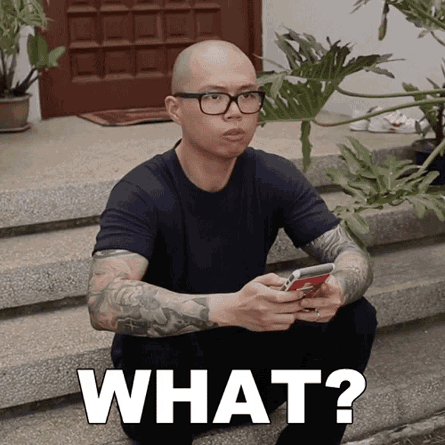 a man is sitting on a set of stairs looking at his phone with the words what on the bottom right