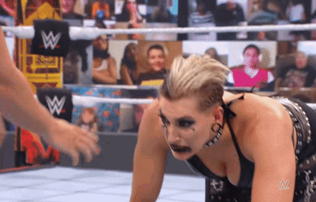 a woman is kneeling down in a wrestling ring with a w logo on the ring .