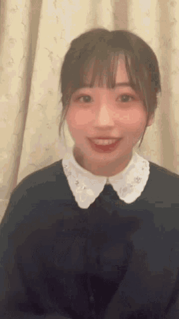 a girl wearing a black sweater and a white collar is smiling