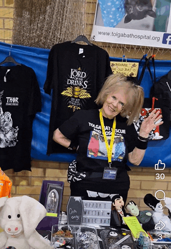 a lady wearing a lord drinks shirt stands in front of a table