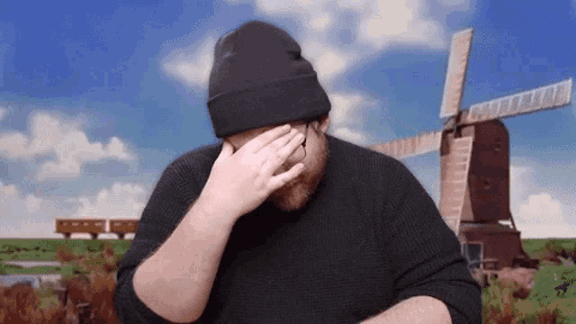 a man covering his face with his hand in front of a windmill .