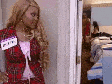 a woman wearing a name tag that says hottie is standing in a room with a bed .