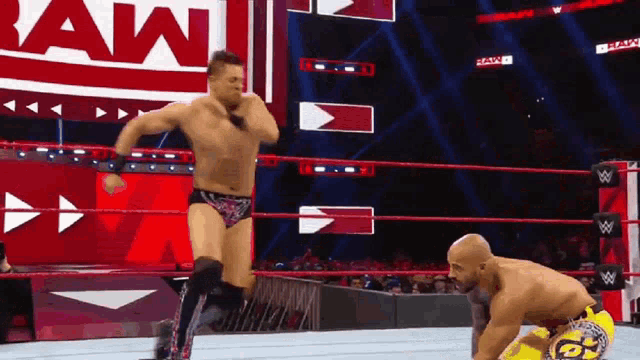 two men are wrestling in a wrestling ring with the word raw on the wall behind them .