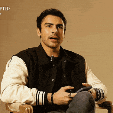 a man in a varsity jacket is sitting in a chair with the word adopted on the bottom