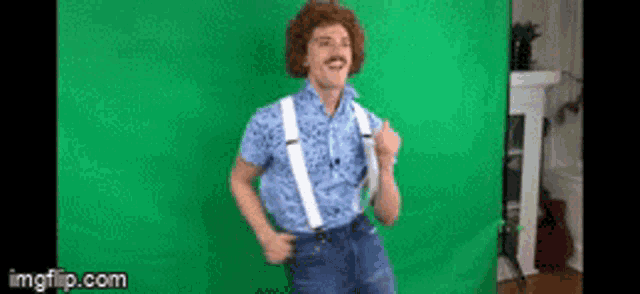 a man wearing suspenders and a blue shirt is dancing in front of a green screen .