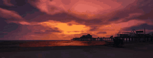 a sunset over a beach with a lifeguard tower in the foreground