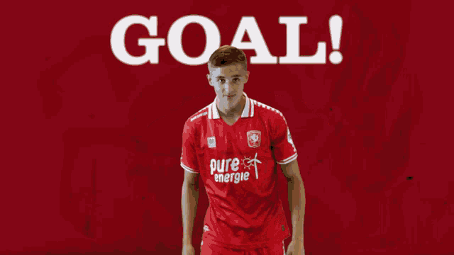 a soccer player wearing a red pure energie jersey points at the goal
