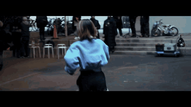 a woman in a blue shirt and black pants stands in front of a group of people
