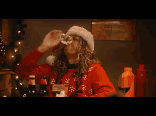 a man wearing a santa hat and a red sweater is holding a glass