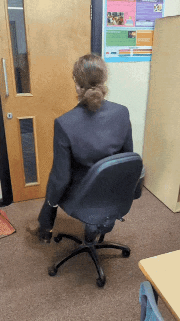 a woman is sitting in a chair in front of a door with a poster on the wall