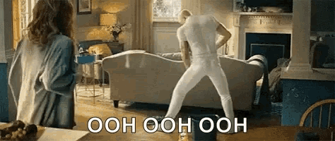 a man is dancing in a living room while a woman watches .