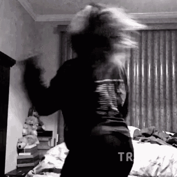 a black and white photo of a person dancing in a bedroom with a bed in the background .