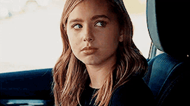 a young girl is sitting in the back seat of a car and making a funny face .