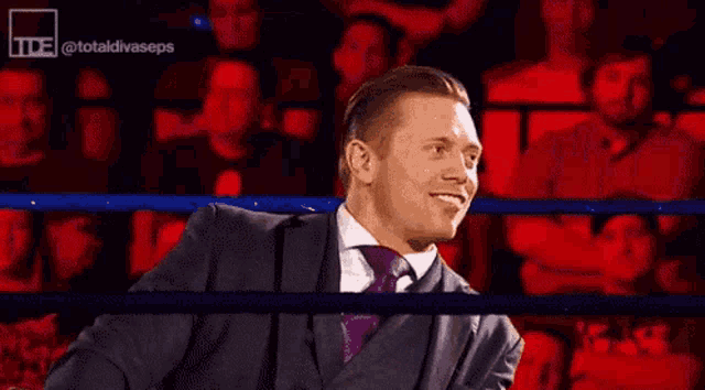 a man in a suit and tie is standing in a boxing ring and giving the middle finger .