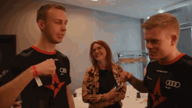 a man wearing an audi shirt talks to another man and a woman