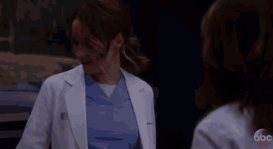 a woman in a lab coat and scrubs talking to another woman .