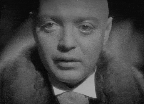 a bald man in a tuxedo and fur coat is looking at the camera .