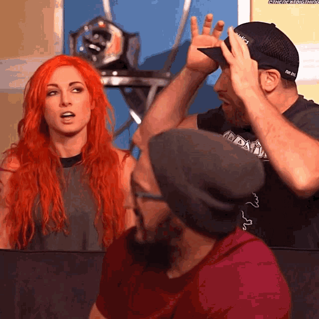 a man wearing a hat that says ' nbc ' on it stands next to a woman with red hair
