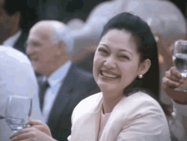 a woman in a white jacket smiles while holding a glass of water