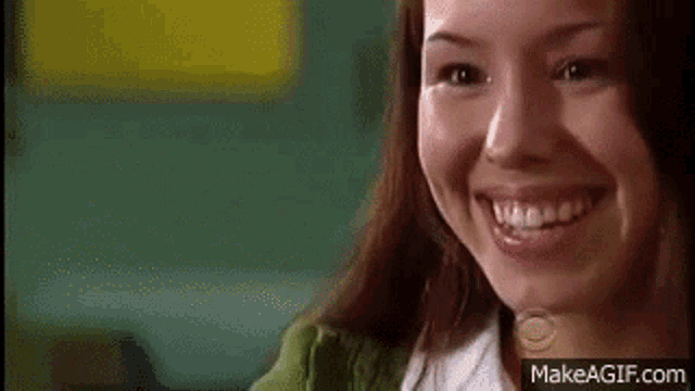 a close up of a woman smiling and looking at the camera on make a gif .