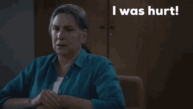 a woman in a blue shirt is sitting at a table with the words i was hurt above her