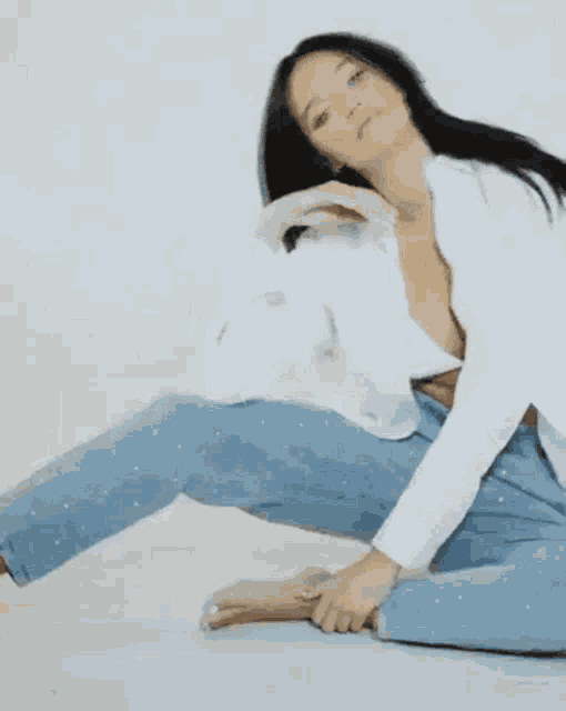 a woman is sitting on the floor wearing a white jacket and blue jeans .