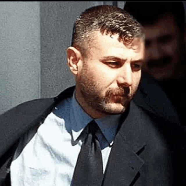 a man with a beard wearing a suit and tie looks at the camera