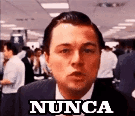 a man in a suit and tie is standing in front of a crowd and says nunca .