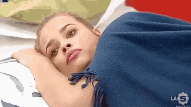 a woman is laying on a bed with a blue blanket and a la 5 logo in the background