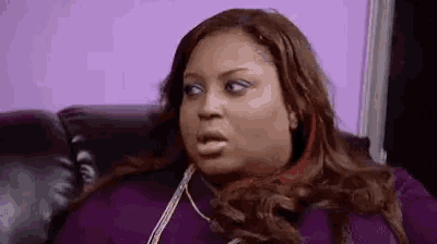 a woman is sitting on a couch making a funny face while talking on a cell phone .