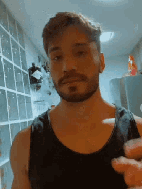 a man with a beard is wearing a black tank top in a kitchen