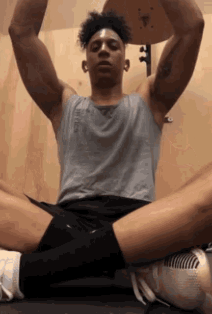 a man sitting on the floor with his legs crossed wearing a grey tank top that says ' nike ' on the front
