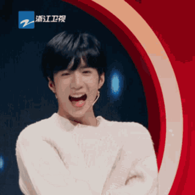 a young man in a white sweater stands in front of a red circle with the letter z on the bottom