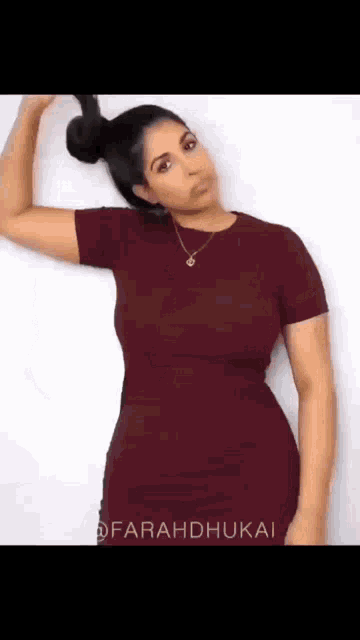 a woman in a burgundy dress is holding her hair in a bun .