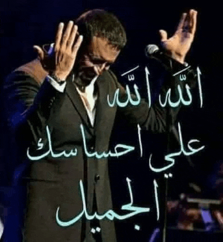 a man in a suit is singing into a microphone with his hands up in the air .