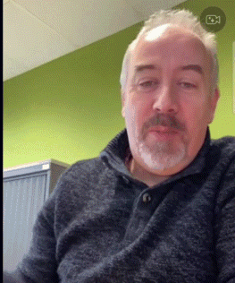 a man with a beard wearing a grey sweater is looking at the camera