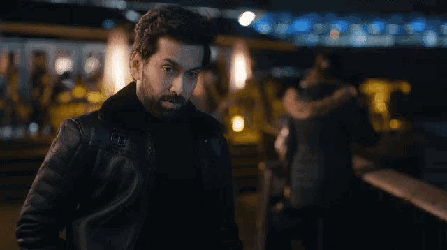 a man with a beard wearing a black leather jacket looks at the camera