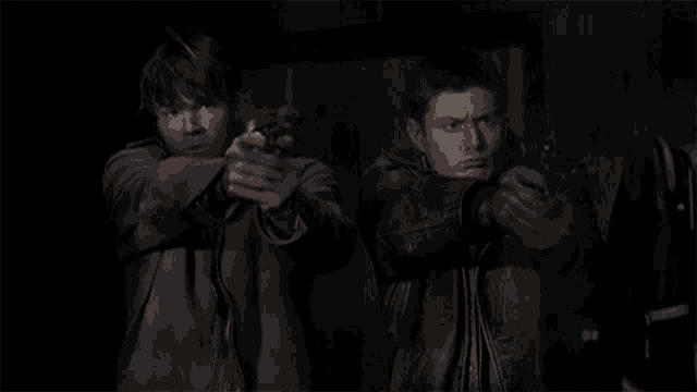 two men in leather jackets are pointing guns at something