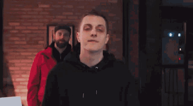 a man in a black hoodie is standing in front of a group of men in red hoodies .