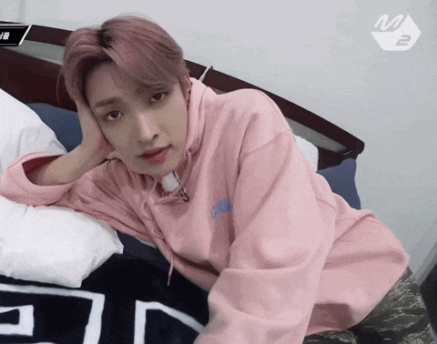 a young man in a pink hoodie is laying on a bed with his head on his hand .